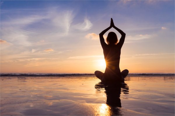 Person meditating in a yoga pose on a beach at sunset